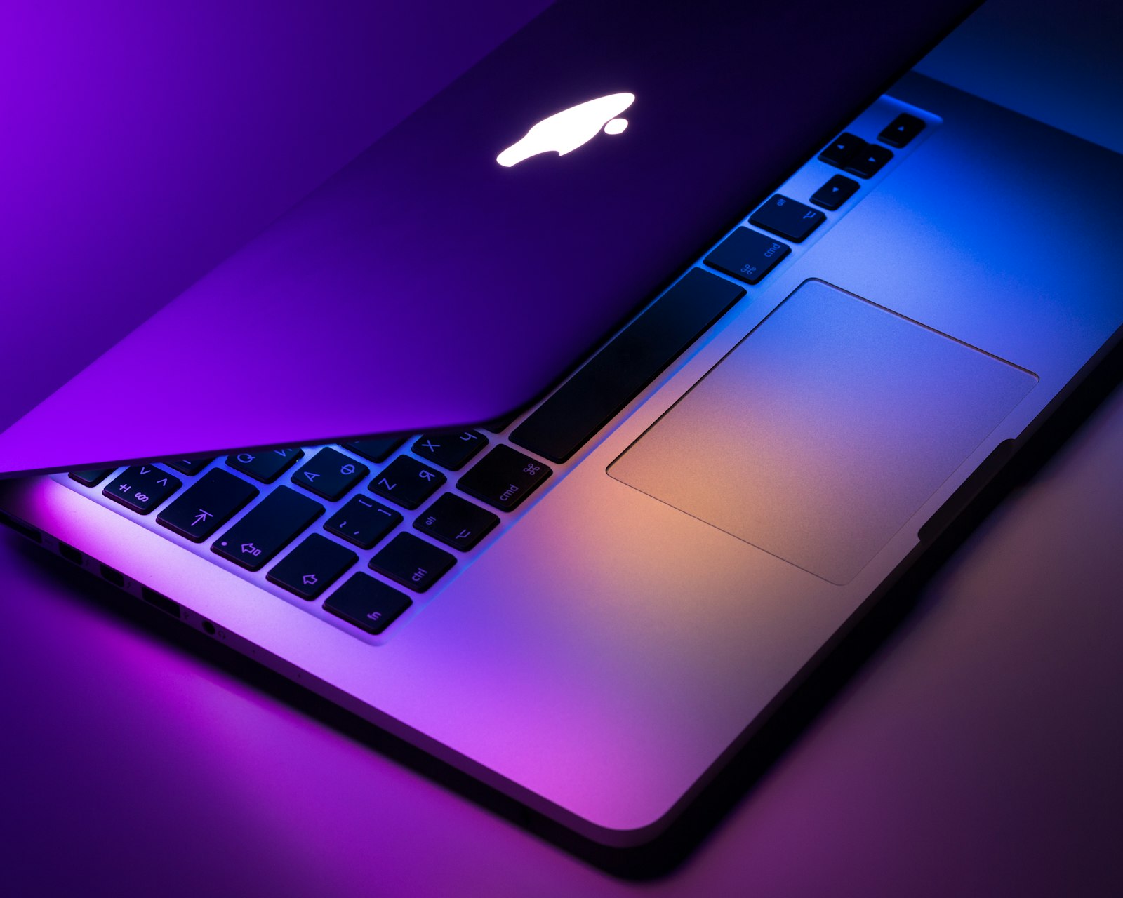 Open silver MacBook with keyboard and trackpad in violet studio light