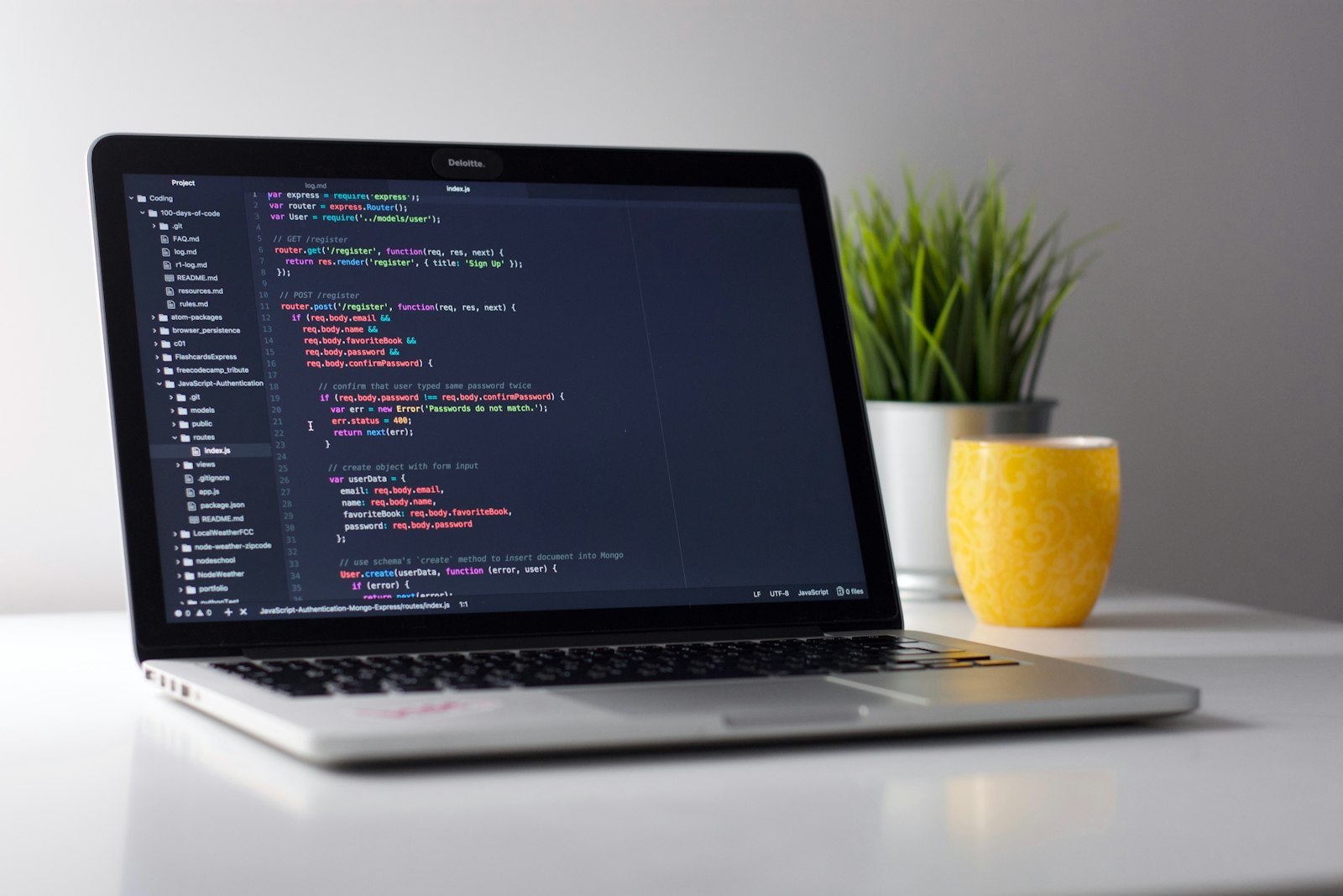 Silver MacBook showing a code editor beside a yellow cup