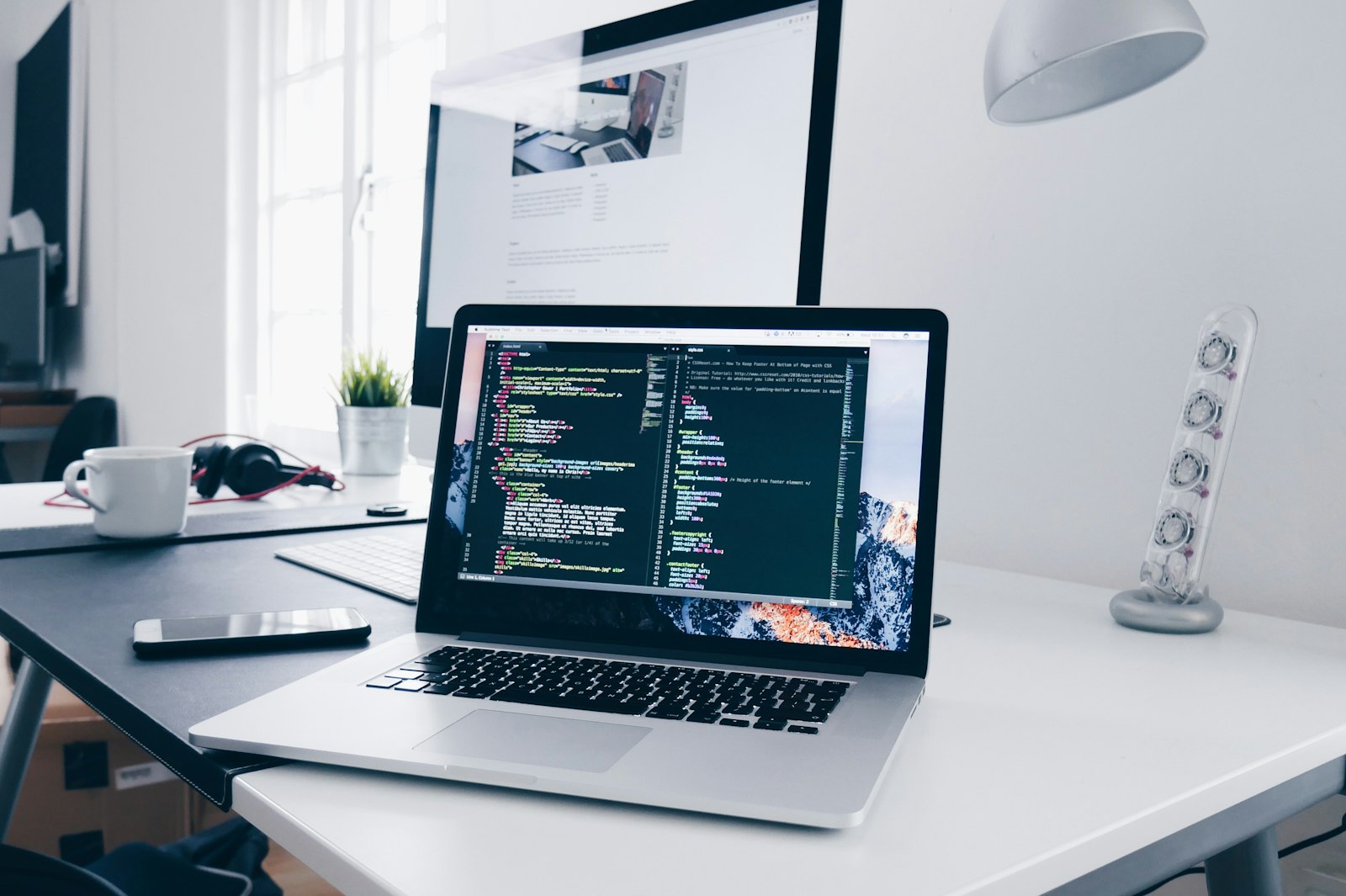 Laptop on a desk with code on the screen and a plant nearby