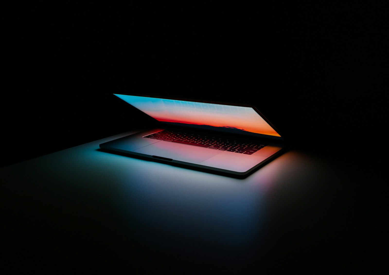 MacBook Pro slightly open with a sunset wallpaper glowing in a dark room
