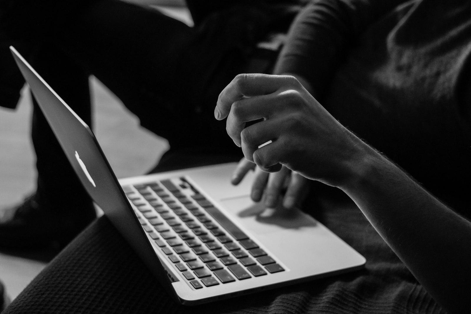 Black and white photo of hands on a MacBook trackpad