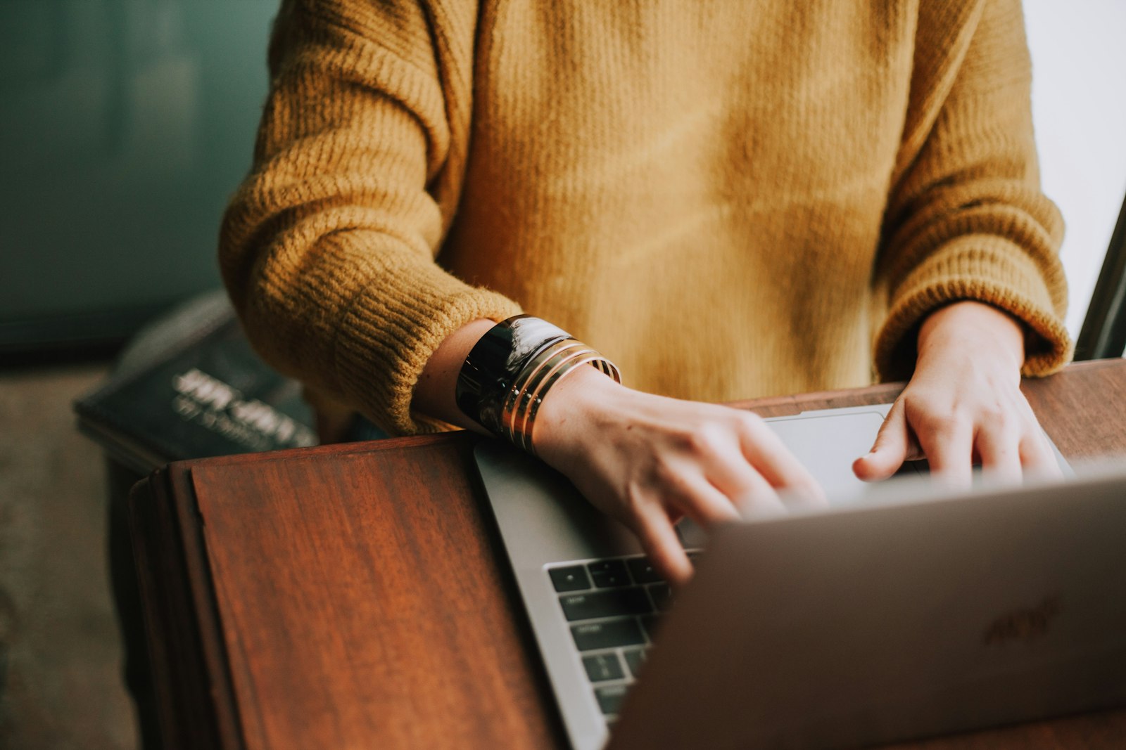 Person in a knit sweater typing on a silver laptop