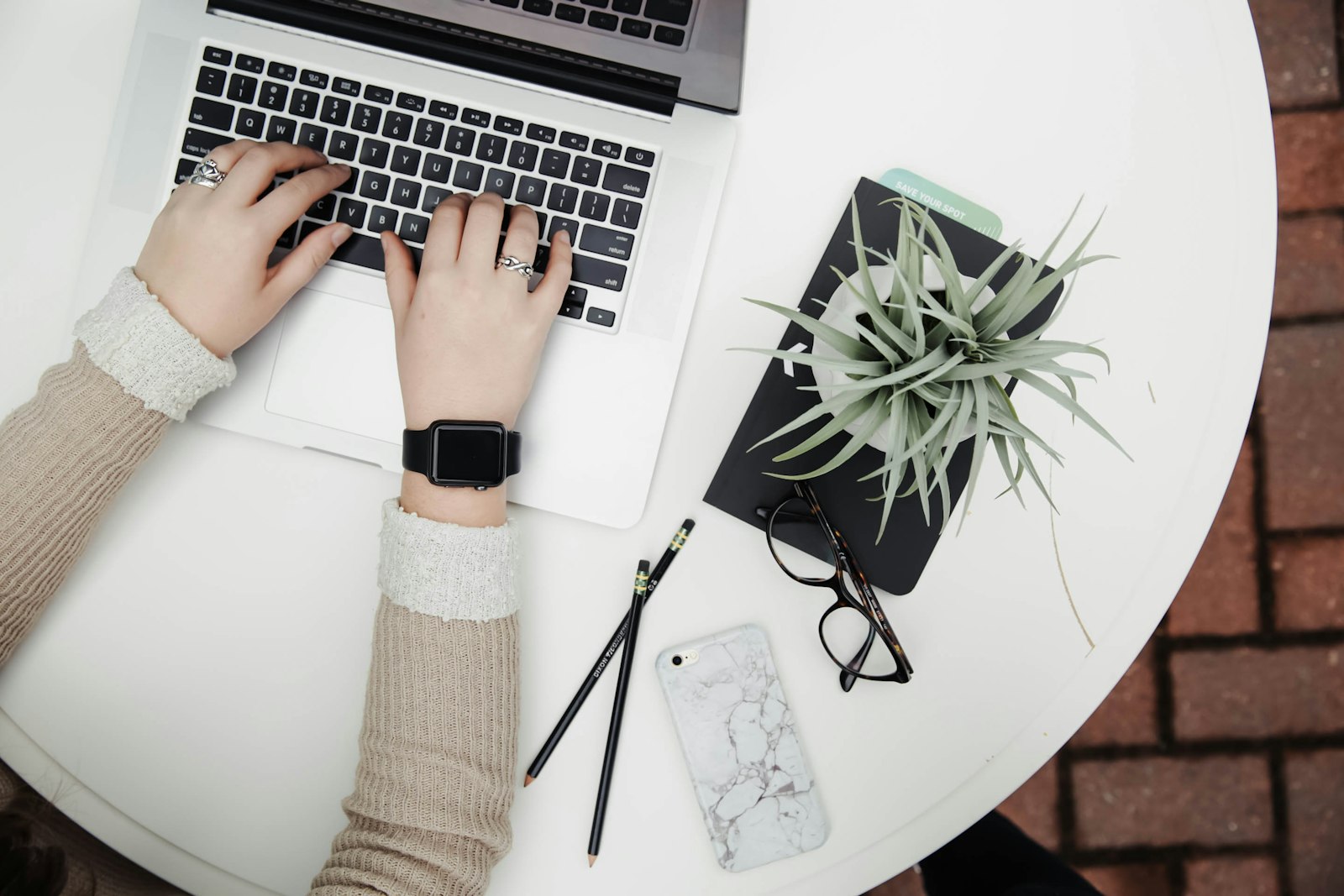 Overhead view of hands typing on a MacBook beside a plant