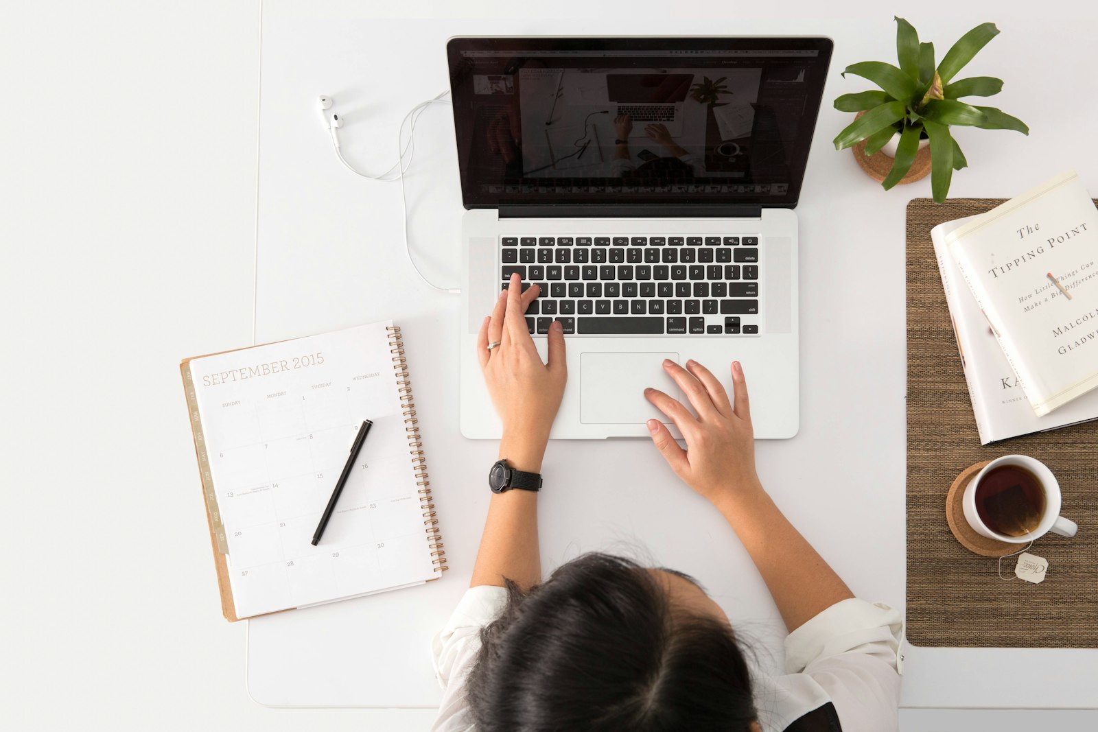 Person using a MacBook at a white desk with a planner